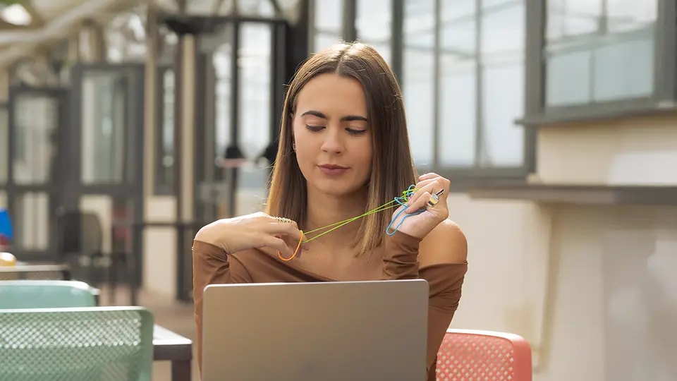 Woman staring at laptop whilst playing with colourful elastic bands