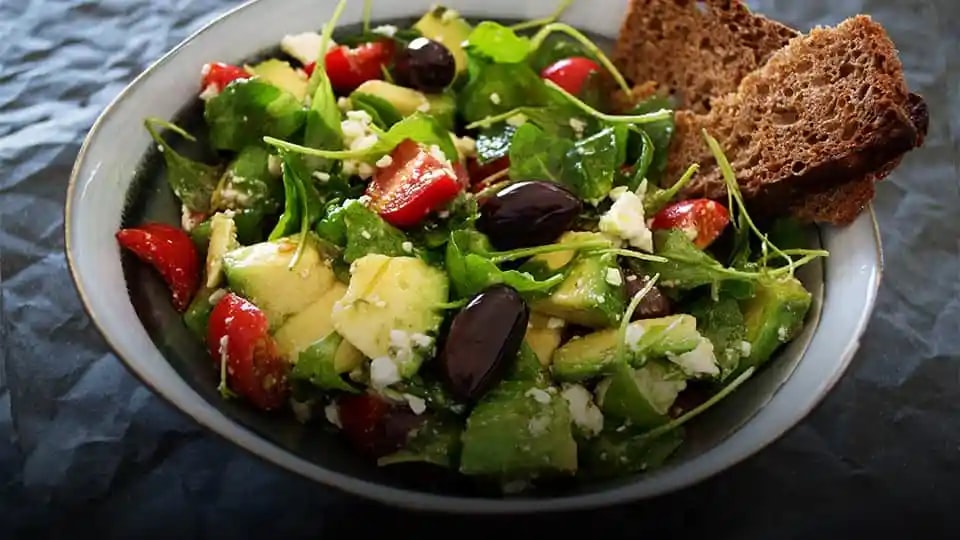 Bowl of salad with green leaves, avocado and olives