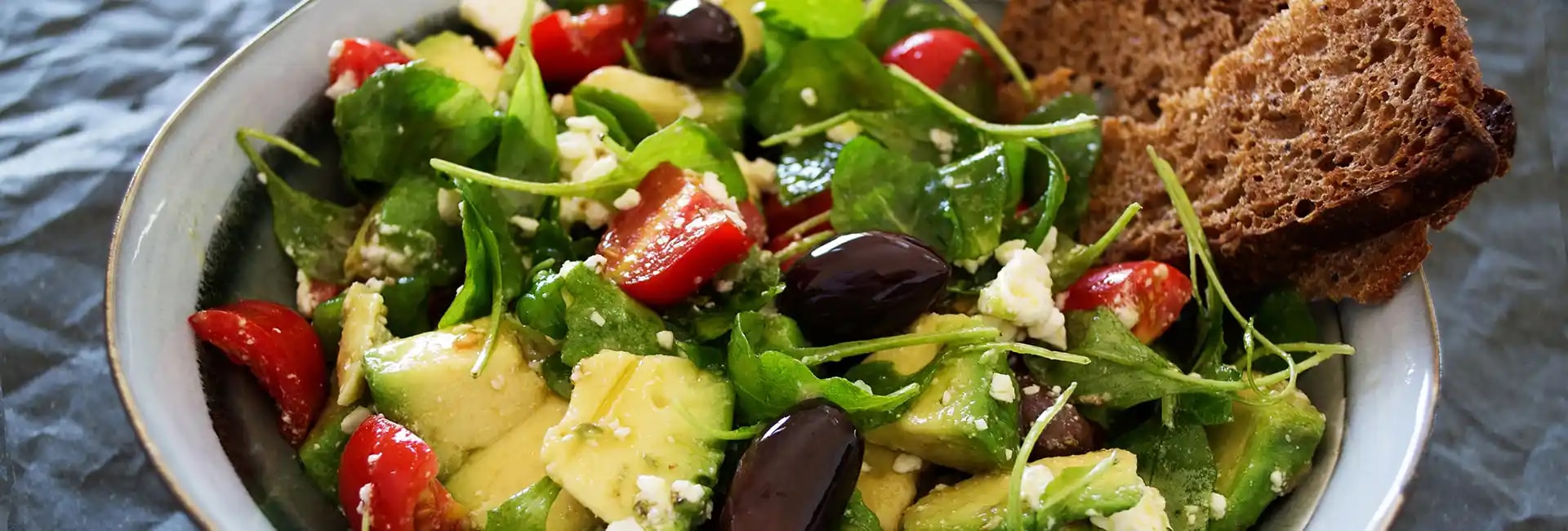 Bowl of salad with green leaves, avocado and olives