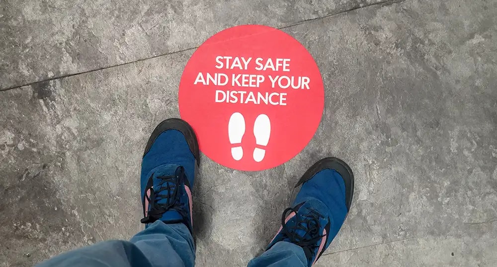 Shoes on a pavement around a Covid Keep your distance sign