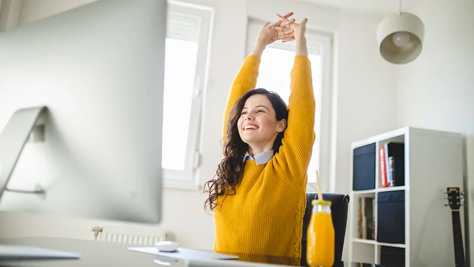 Woman working from home stretching her arms in front of her computer