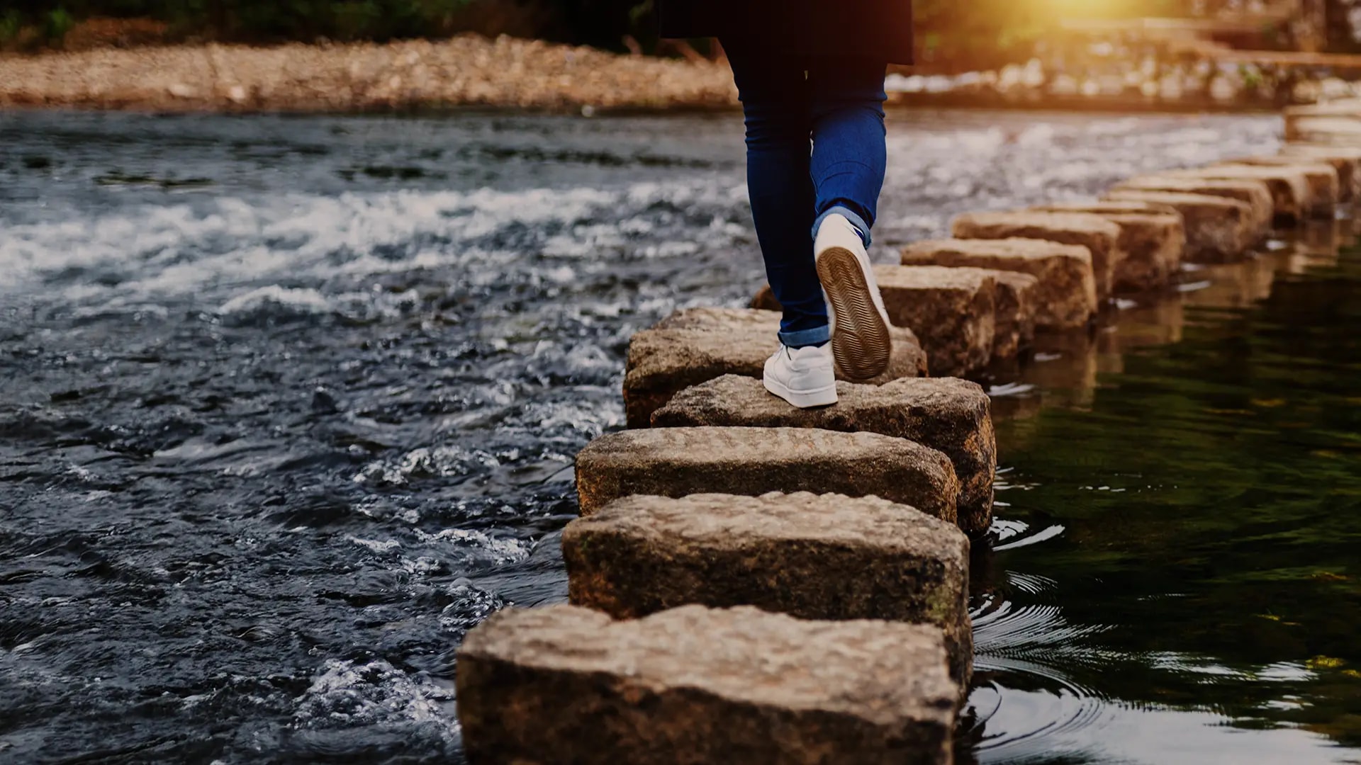Person stepping on stones crossing a river